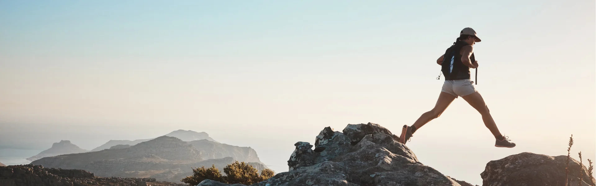 Frau springt sportlich über Felsen bei Sonnenuntergang – Minerva-Vita Longevity Supplements für mehr Energie, Zellgesundheit und ein gesundes Altern.