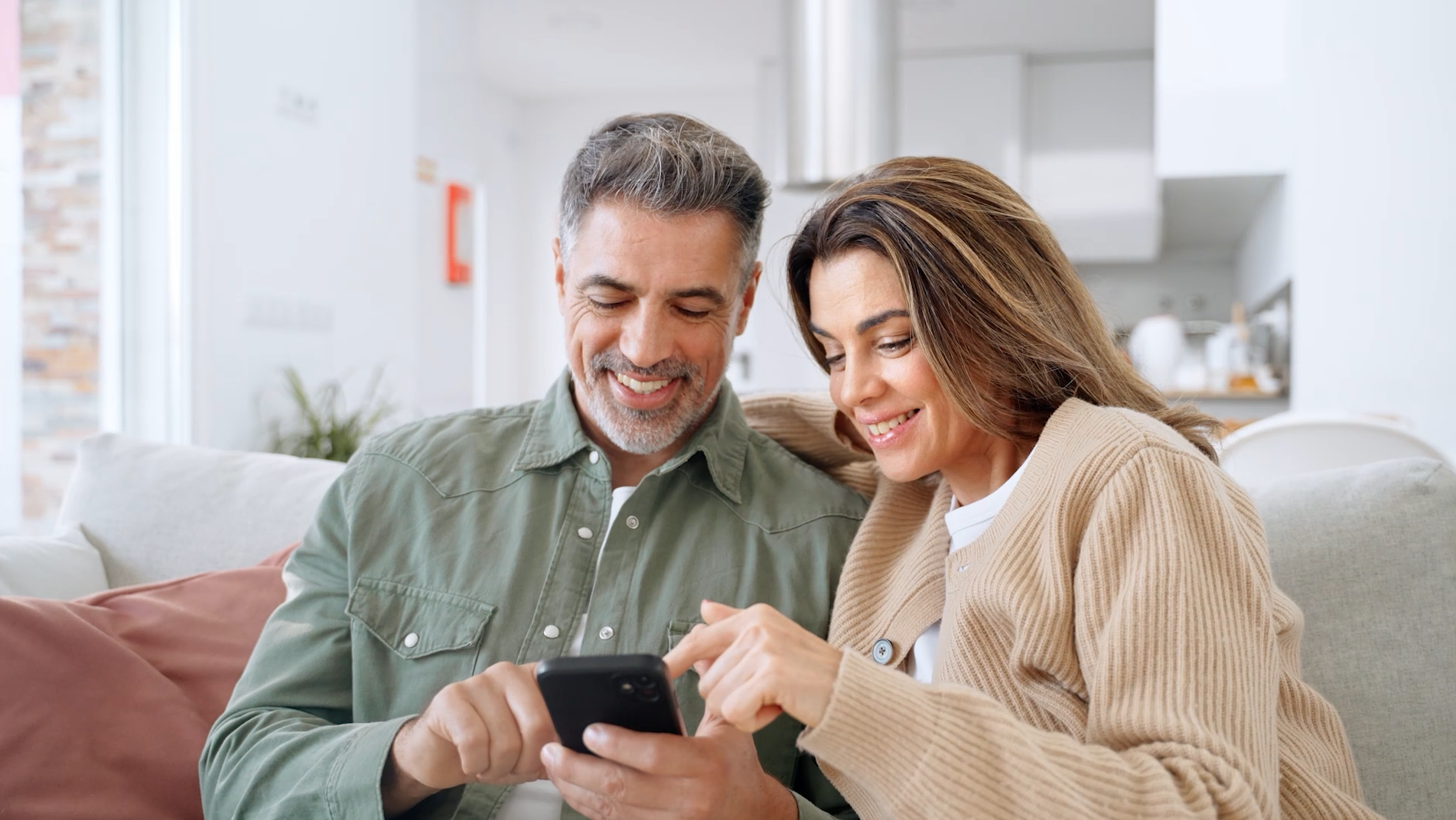 Lachendes Paar auf dem Sofa blickt gemeinsam auf ein Smartphone – Symbol für Energie, Vitalität und gesunde Zellen durch Longevity-Supplements von Minerva-Vita.