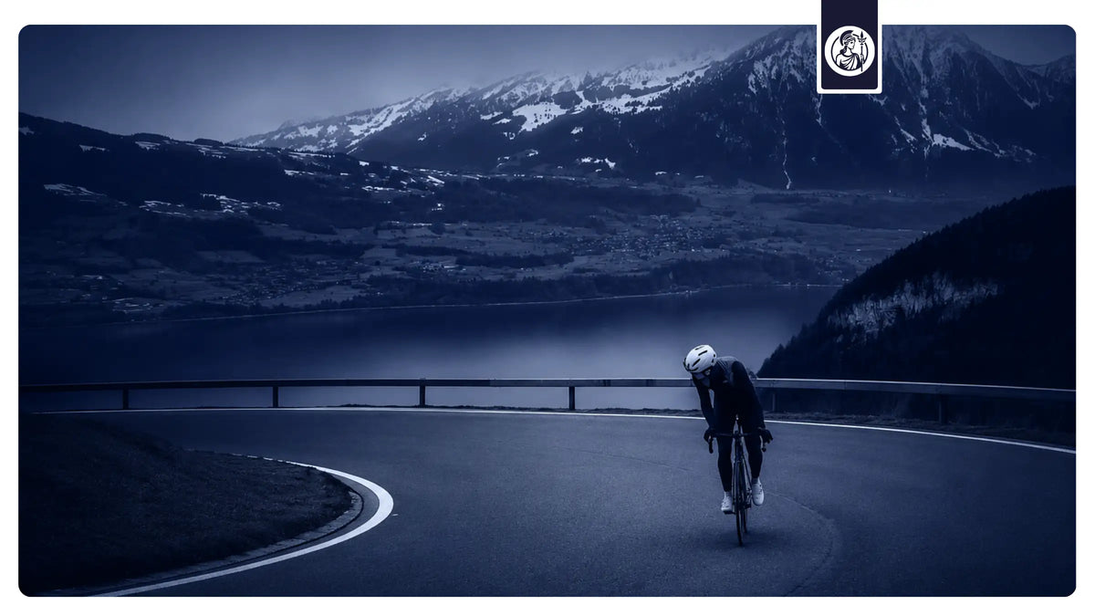 Sportlicher Radfahrer auf einer kurvigen Bergstraße vor eindrucksvoller Alpenkulisse und See