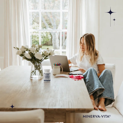 Frau arbeitet am Laptop, während Minerva-Vita LUMA Carotin E Kapseln auf dem Tisch stehen.
